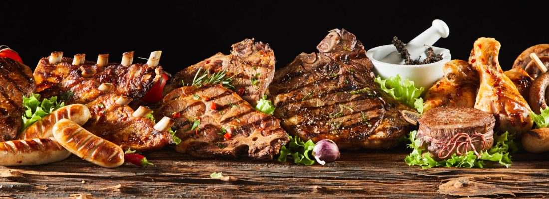 A selection of various barbecued gourmet meats on a rustic timber board with a black background.